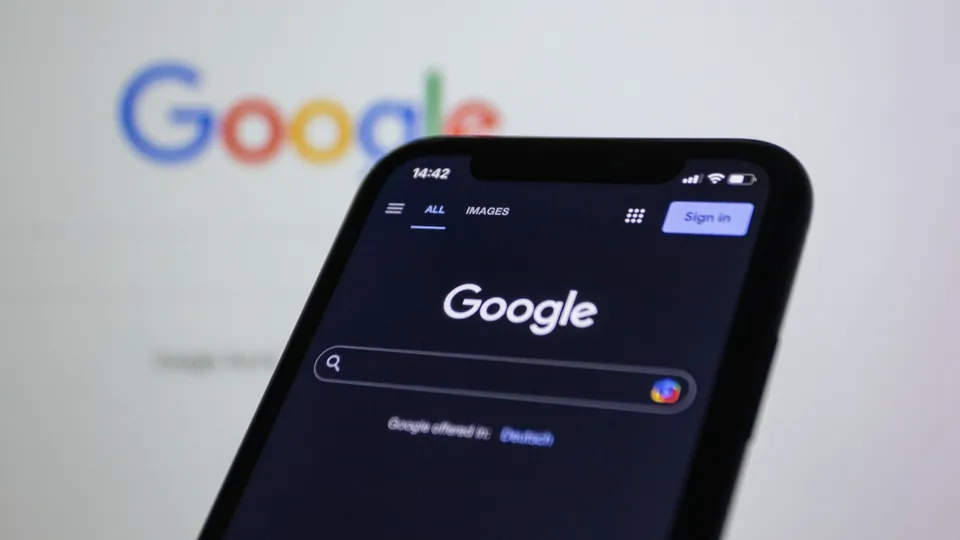 Buscador de Google en un teléfono frente a una pantalla de computadora.